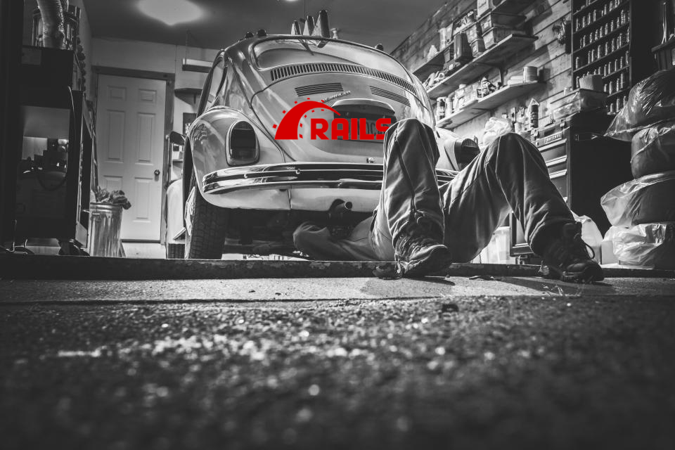 A mechanic is under a Volkswagen Beetle giving maintenance to the engine.